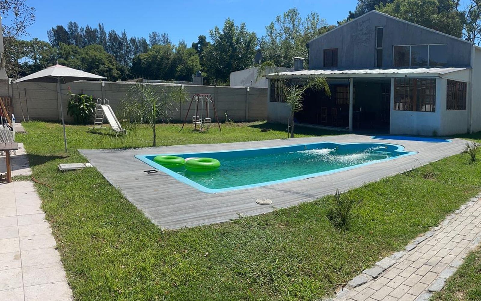 Pileta con deck de madera, parque con juegos para chicos y galería techada al fondo